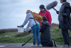 Three teenagers on a beach using film equipment.