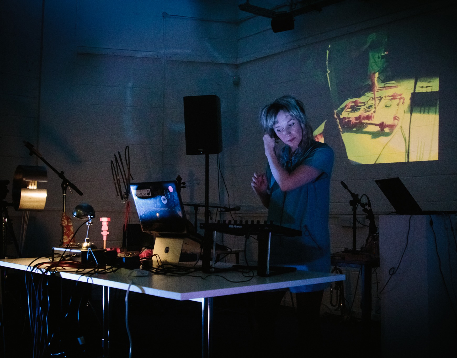 Sound artist Vicky Clarke performs on sound desk in dark room with video projections