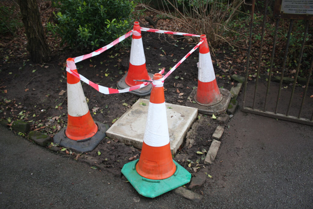 A colour photograph of four traffic cones with orange and white striped tape attached to the four cones in a square arrangement.