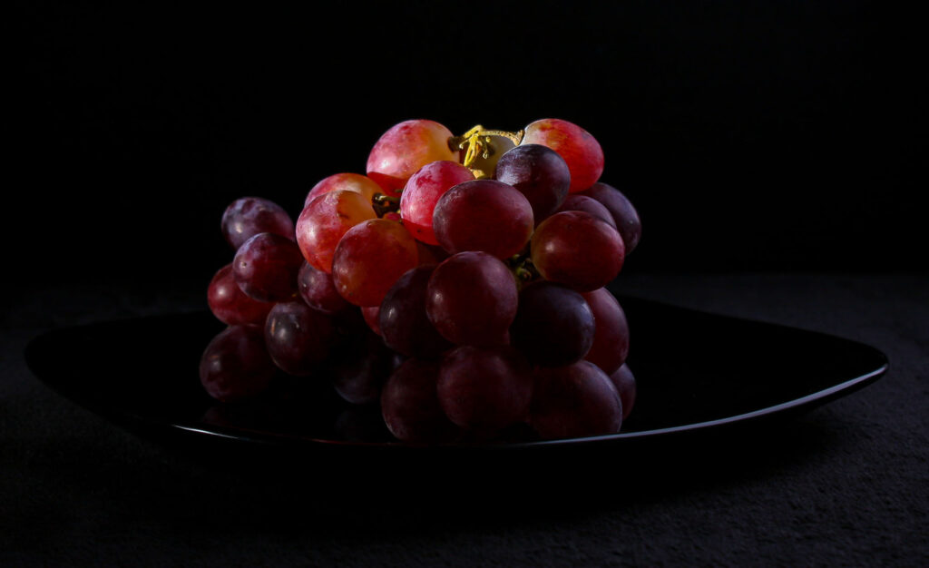 A close up still life photograph of grapes on a black plate. Spotlit from the side.