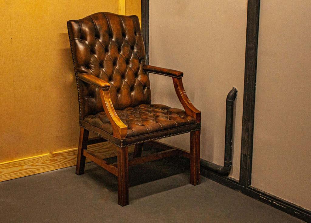 A colour photograph of a brown leather chair in the corner of a room.