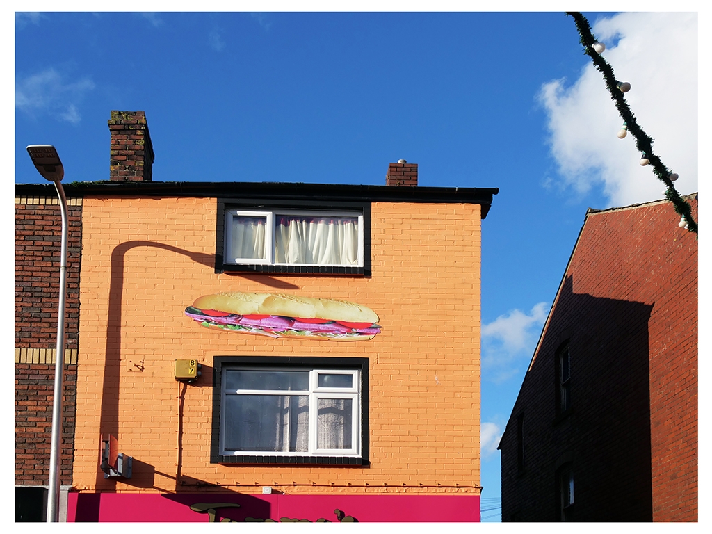 A colour photograph of a building with an orange painted facade with a large picture of a sandwich stuck to the facade.