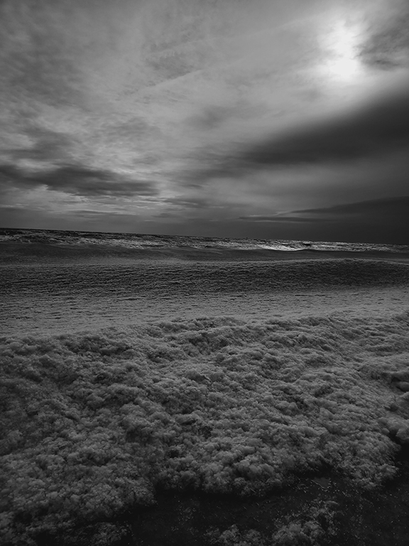 A black and white photograph of sea foam along the west coast of cumbria.