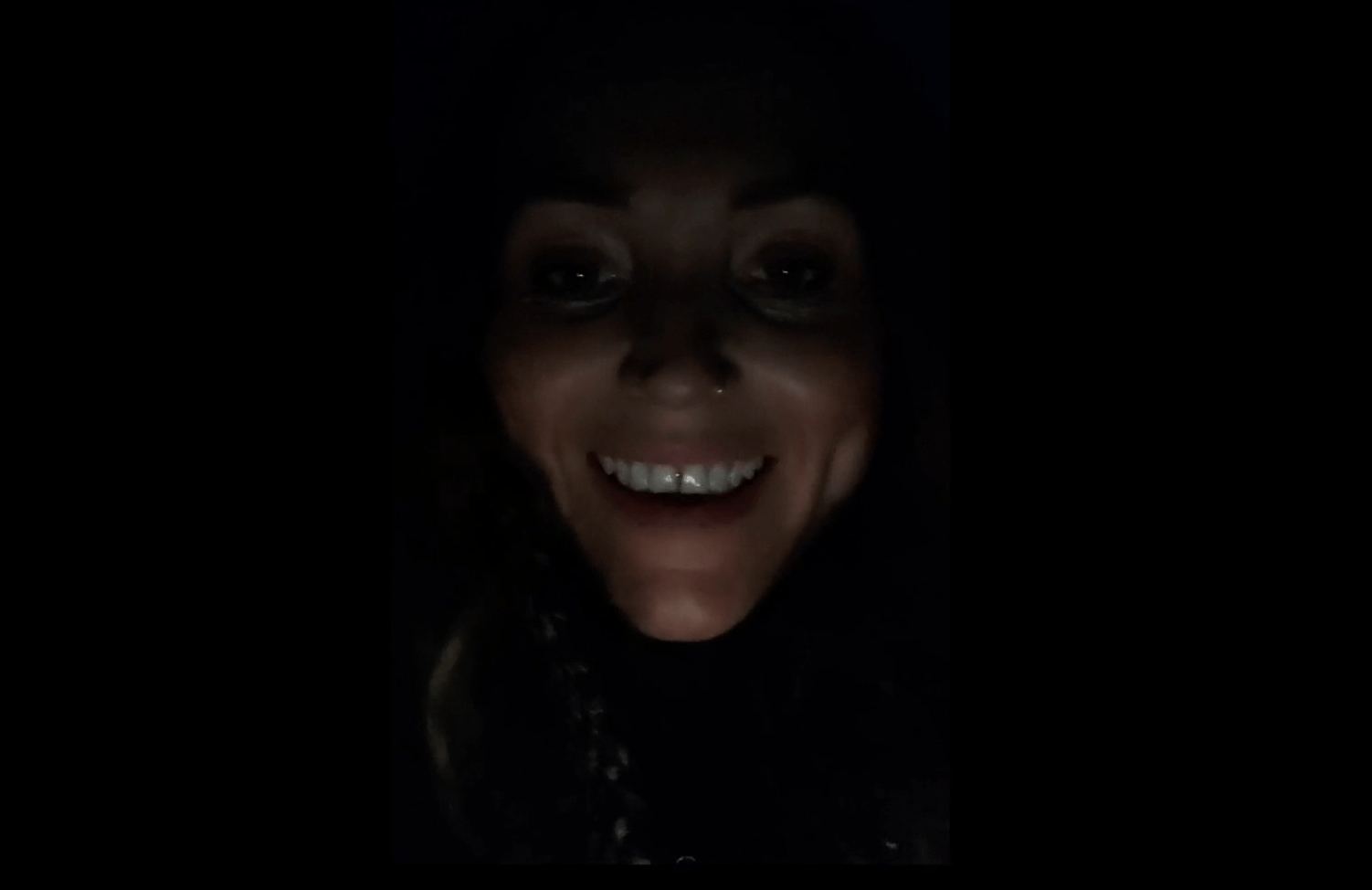 A photograph of a smiling woman's face in the dark
