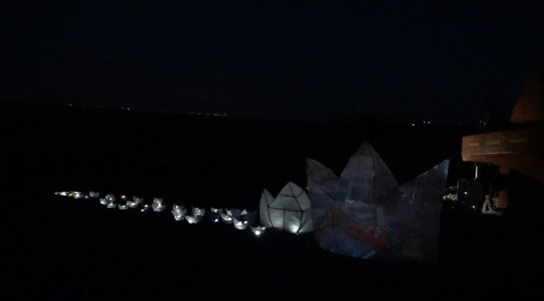 A photograph showing lots of small paper boats lit up in the dark, arranged in a row.