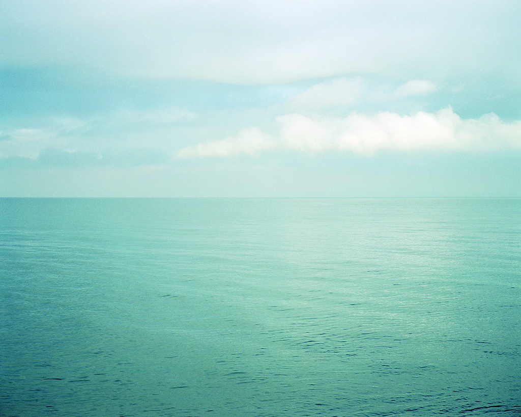 A colour photograph of the blue sea with a blue sky with clouds.