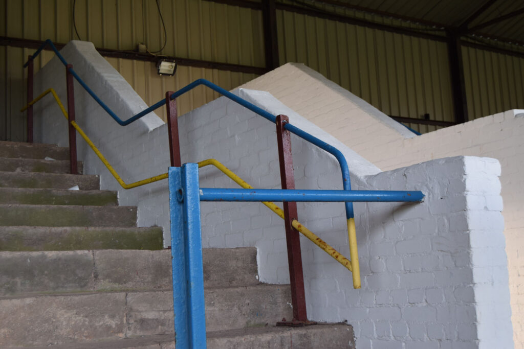 A colour photograph of some cement stairs with a blue, red and yellow metal handrail.