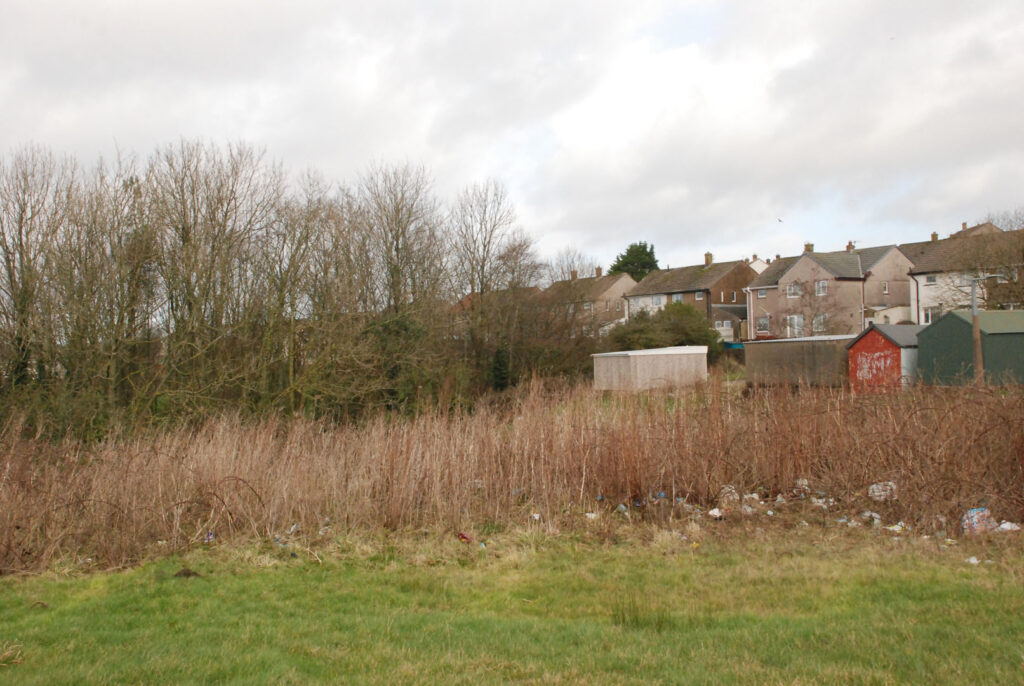 A colour photograph of some green open space with some houses in the background.
