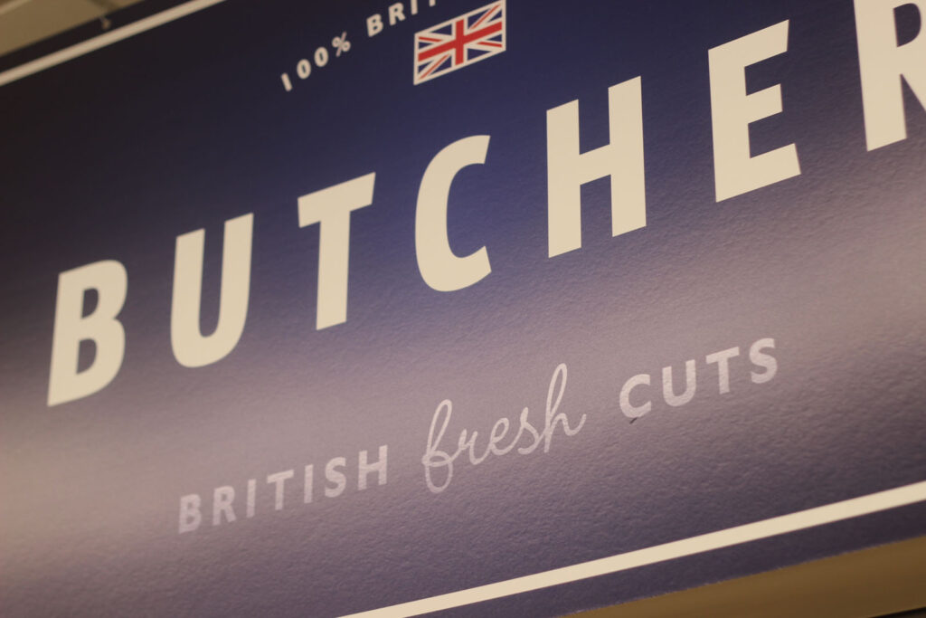 A close up colour photograph of a blue sign with white writing which says '100% british butchers, british fresh cuts"