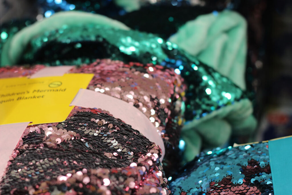 A colour close up photograph of folded sequin blankets in pink, blue and green colours.