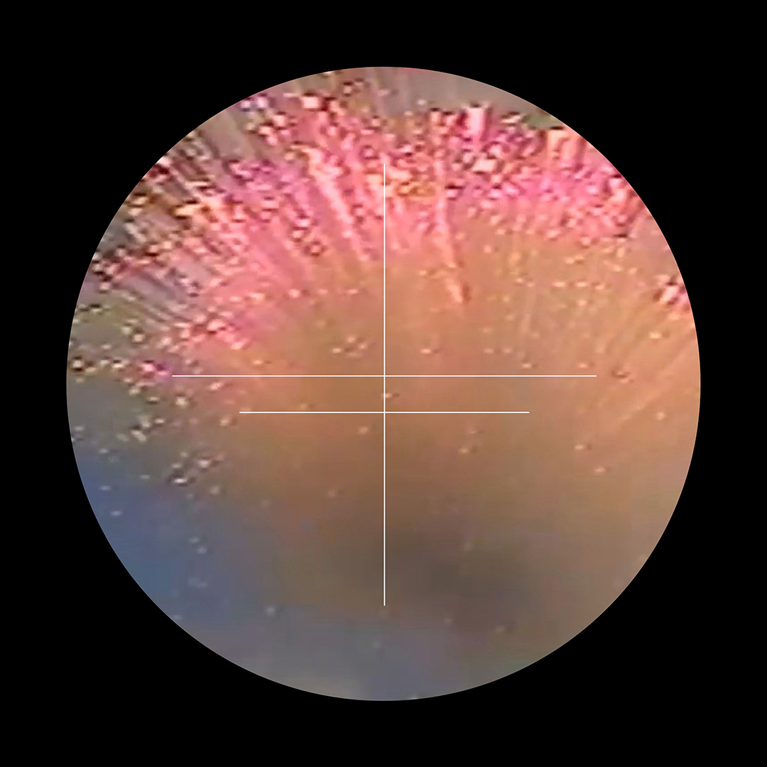 A colour photograph of a red and orange explosion. Set within a black circle. Over the top of the explosion photograph is a white cross.