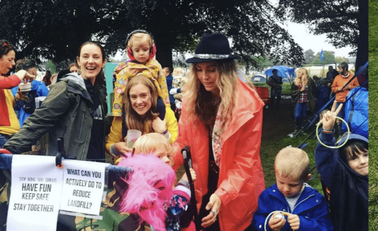 A photo of a woman smiling in a hat, surrounded by children and holding up a placard