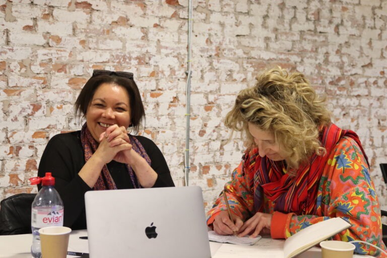 Previous creative workshop. Two participants are smiling and one is writing